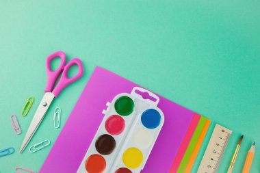 Okul malzemeleri, makas, kağıt, suluboya resimler, fırça, kalem ve cetvel yeşil arka planda