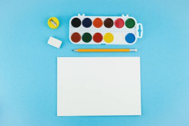 Okul geçmişine, farklı okul malzemeleriyle dönüş. Manzaralı. Suluboya paleti, renkli kalemler ve boya için fırça.