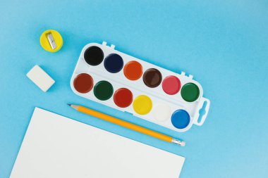 Okul geçmişine, farklı okul malzemeleriyle dönüş. Manzaralı. Suluboya paleti, renkli kalemler ve boya için fırça.