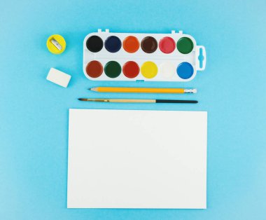 Okul geçmişine, farklı okul malzemeleriyle dönüş. Manzaralı. Suluboya paleti, renkli kalemler ve boya için fırça.