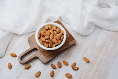 Tahta bir tahtanın üzerinde beyaz kumaşla bir kâsede tam badem.