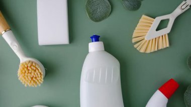 Yeşil bir yüzeye yerleştirilmiş şişe ve fırçaları içeren beyaz temizlik malzemeleri.