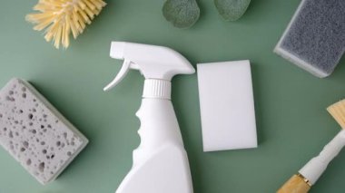 Yeşil arka planda temizlik süngeri ve fırça ile beyaz sprey şişe