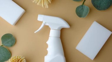 Açık kahverengi arka planda yeşil yapraklı temiz fırçalar ve süngerlerle beyaz sprey şişesi..