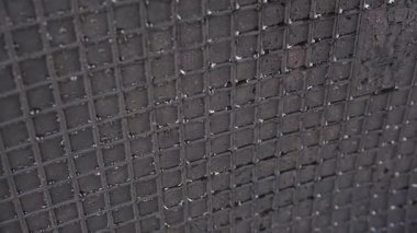 Endüstriyel desenli kaba bir yüzey üzerinde çok sayıda küçük su damlacıklarını gösteren soyut koyu metal şablonun yakın görüntüsü.