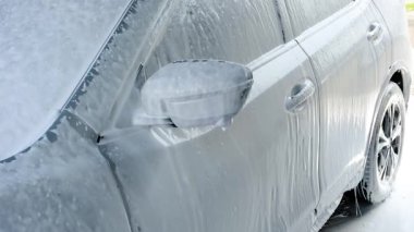 Kalın beyaz sabun köpüğüyle kaplı temiz bir araç. Yan ayna ve kapı kolu köpükle kaplı. Temizleme baloncukları damlıyor.