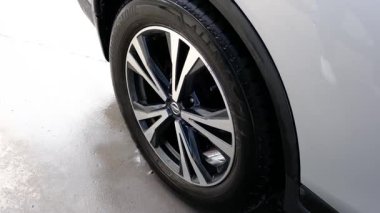 Temiz bir araç tekerleği, siyah bir lastik ve ıslak asfalt üzerinde parlak metal bir kenar. Otomatik ayrıntı.