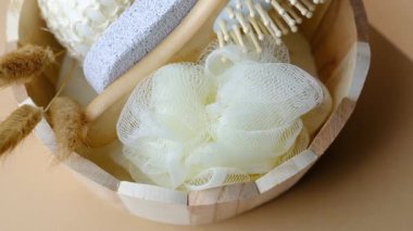 Hafif banyo aksesuarları, yumuşak bir banyo şişmesi, deri yüzen taş ve rahatlamak için ahşap fırça da dahil olmak üzere ahşap bir kovada düzenlenir..