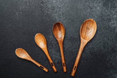 Koyu bir taş yüzeyde düzgün dizilmiş çeşitli tahta kaşıklar..