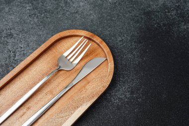 Çatal ve bıçak düzgün bir şekilde ahşap bir tepsiye yerleştirilmiş koyu renkli bir yüzeye karşı.