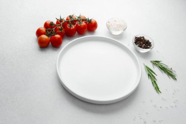 Beyaz arka planda tuz, biber, domates ve biberiye ile boş beyaz tabak