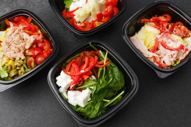 Restoran teslimatı ya da yemek hazırlama konsepti için siyah kaplarda taze sebzelerle karışık salatalar et peyniri ve yeşillikler.