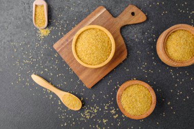 Kaşık ve arka planda çatlamış buğday lapası taneleri olan bir sürü kase. Sağlıklı Çiğ Tahıl Taneleri.