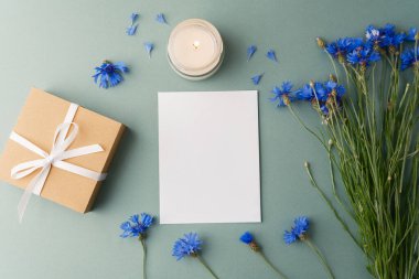 Yeşil arka planda çiçek olan hediye kutusu, mum ve kart