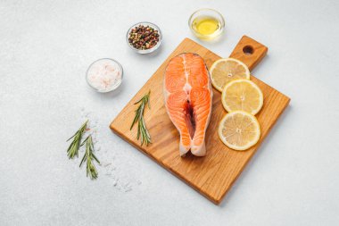 Limon dilimleri ve baharatlarla birlikte kesme tahtasına yerleştirilmiş somon filetosu.