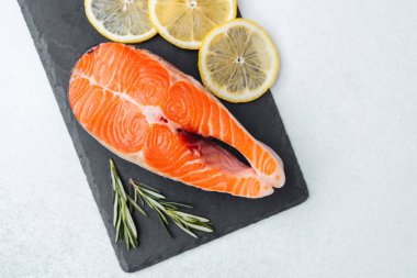 Taze limon dilimleri ve biberiye filizleriyle süslenmiş parlak somon biftekleri..