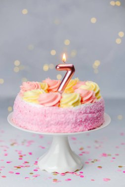 Yedi numaralı mumlu canlı bir doğum günü pastası beyaz bir stantta oturur..