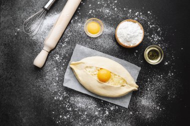 Çiğ khachapuri, yumurta sarısı ve parşömen üzerinde peynir ve siyah arka planda un.