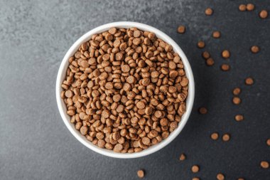 Siyah arka planda kuru köpek mamasıyla dolu beyaz kase ve dağınık mamalar.