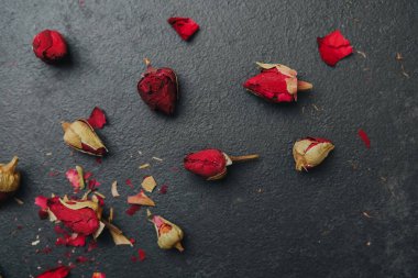 Koyu desenli bir yüzeye serpilmiş yapraklı kurumuş gül goncaları..