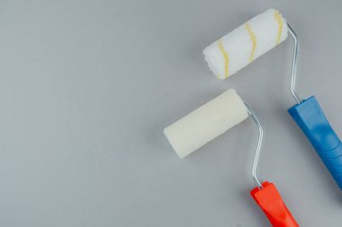 Ev geliştirme ve DIY boyama konsepti için gri arka planda kırmızı ve mavi saplı iki boya silindiri.