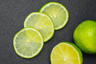 Parlak yeşil kireç dilimleri ve koyu renkli bir yüzeye sergilenmiş bir kireç..