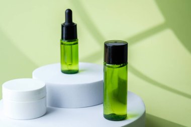 Dairesel kaide üzerine sergilenen yeşil kozmetik şişesi ve beyaz krema kavanozları