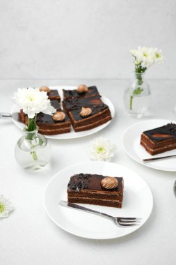 Zengin çikolatalı kekler beyaz tabaklarda servis ediliyor taze beyaz çiçekler ve narin krema kıvrımlarıyla..