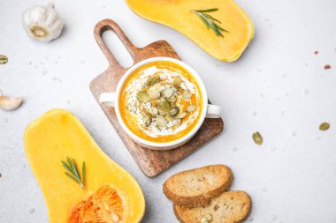 Kremalı kabak çorbası ve ahşap tahtada ekmek ve sarımsaklı kabak tohumu.