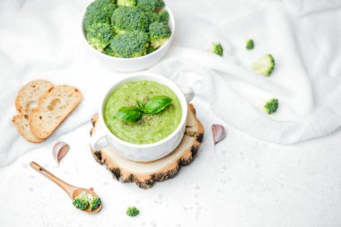 Fesleğenli kremalı brokoli çorbası ve beyaz kumaş arka planda kızarmış ekmek.