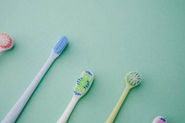 Pastel arka planda düzenlenmiş temiz diş fırçaları, pastel mavi, beyaz, yeşil, pembe renkler.