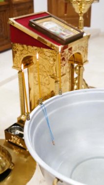 Edebi mumlar ve kutsal ikon vaftiz fontunun yanındaki altın bir stantta su ile birlikte.