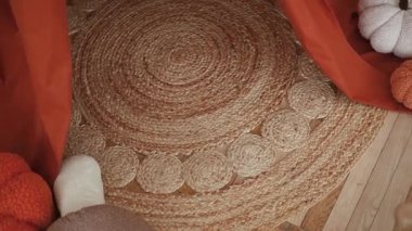 Yuvarlak desenli sıcak jüt halı, sonbahar balkabakları ve ahşap zeminde turuncu kumaş aksanları.