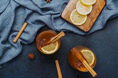Tarçın çubuklu sıcak içecekler, yıldız anason ve mavi kumaşlı limon dilimleri.