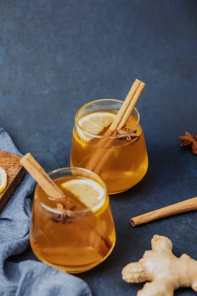 Limon dilimli sıcak içecek, tarçın çubuğu ve bardakta yıldız anason, koyu mavi arka planda servis edilir.