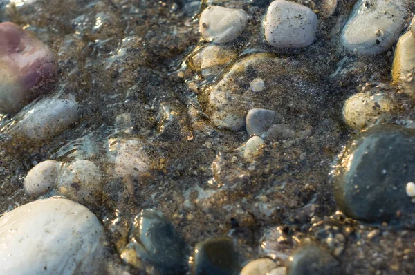 pebble stones on the sea beach on a warm summer day, the rolling waves of the blue sea with white foam