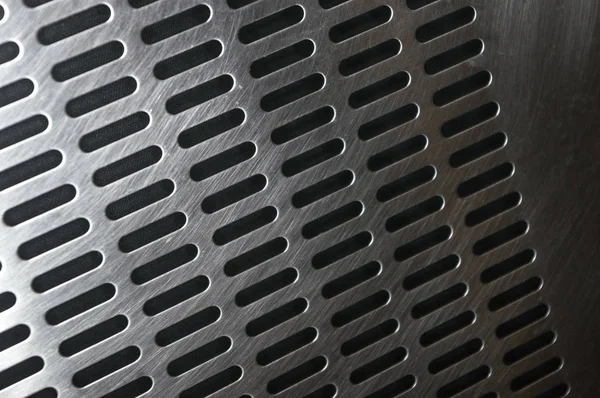 stainless steel grating with oblong holes on black background, close-up