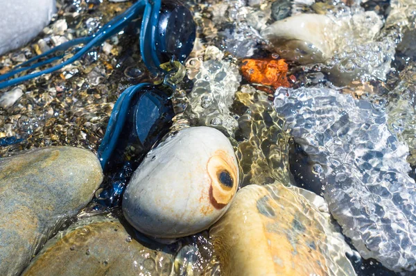 eyeglasses for swimming on a pebble beach in the sea waves, a warm summer day, close-up