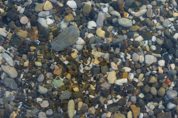 pebble stones on the sea beach on a warm summer day, the rolling waves of the blue sea with white foam