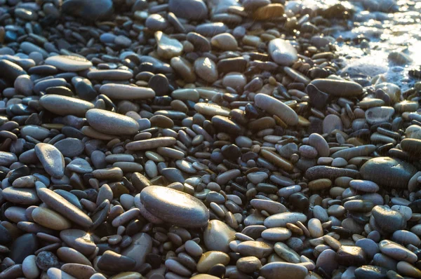 pebble stones on the sea beach on a warm summer day, the rolling waves of the blue sea with white foam