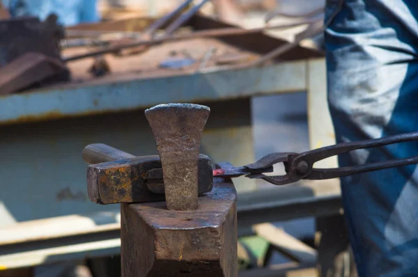 blacksmith performs the forging of hot glowing metal on the anvil, close-up
