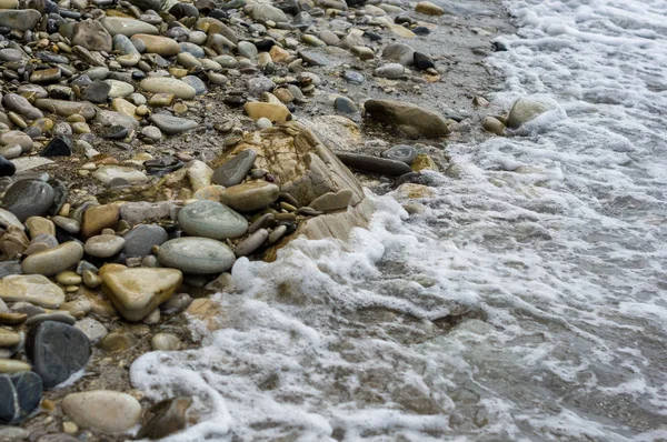 pebble stones on the sea beach on a warm summer day, the rolling waves of the blue sea with white foam