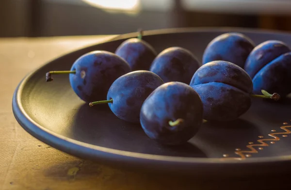 juicy blue plums in ceramic plate on wooden background, close-up