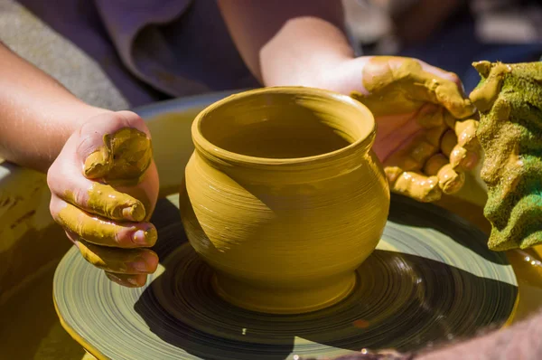 hands of the skilled master Potter and children's hands, training of the kid to production of pottery on a Potter's wheel, close-up