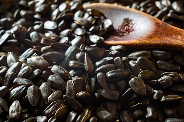 Fried sunflower black seeds with a wooden spoon in a pan, close up