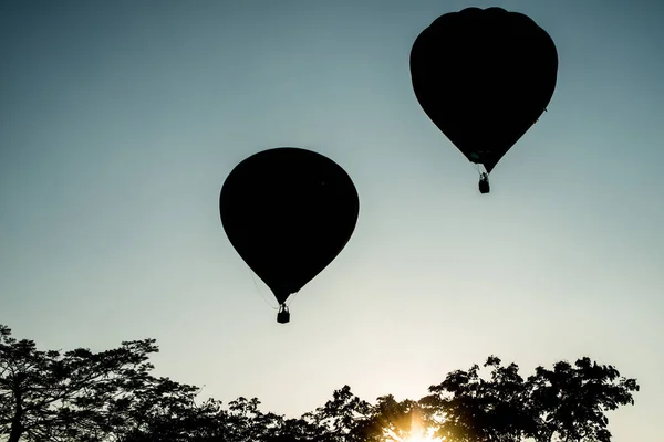 The silhouette of hot air balloons flying up in the sky at evening.
