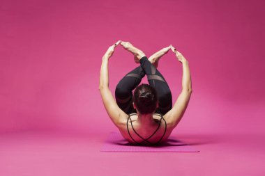 Uzun saçlı güzel pilates ya da yoga atlet bir stüdyoda pembe bir arka plan karşı sıkı spor kıyafeti giymiş süre zarif bir poz mu