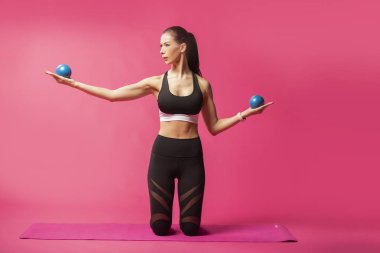 Uzun saçlı güzel pilates ya da yoga atlet bir stüdyoda pembe bir arka plan karşı sıkı spor kıyafeti giymiş süre zarif bir poz mu