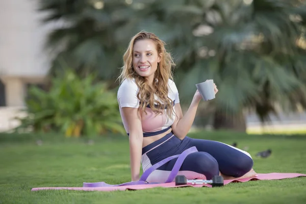 Hermosa Joven Sosteniendo Una Taza Una Esterilla Yoga Parque — Foto de Stock