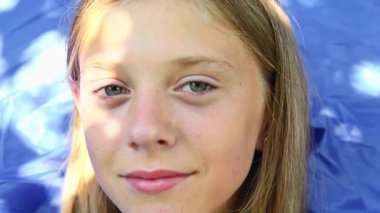 Gülen Mutlu Çocuk. Mavi arka planda gülümseyen 10 yaşındaki bir kızın yakın çekimi. Saf, sınırsız mutluluk duygusu. 10 yaşında, parlak mavi gözlü ve sarı saçlı bir kız..